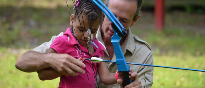 An instructor helps a camper practice archery